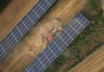 Traktor fährt durch ein Feld, auf dem Photovoltaik-Anlagen stehen