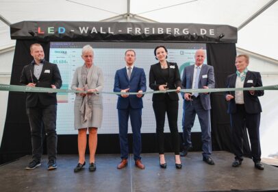 Zdjęcie przedstawia symboliczne przecięcie wstęgi podczas konferencji prasowej z okazji otwarcia największego magazynu energii w Saksonii, należącego do firmy JT Energy we Freibergu
